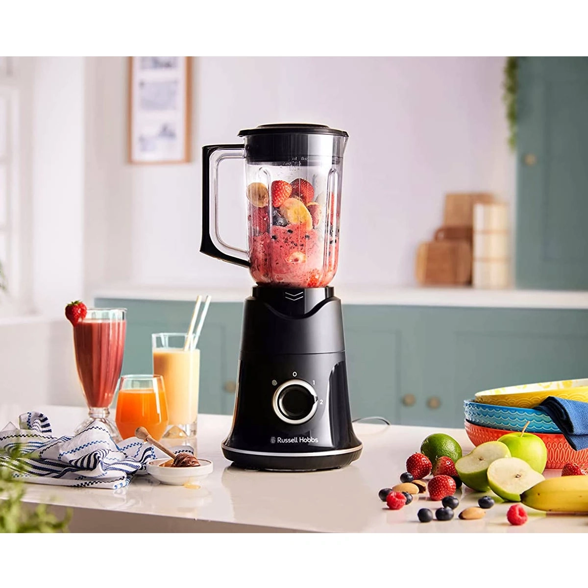 Schwarzer Mixer mit Früchten und Getränken auf einem Tisch mit Obst.