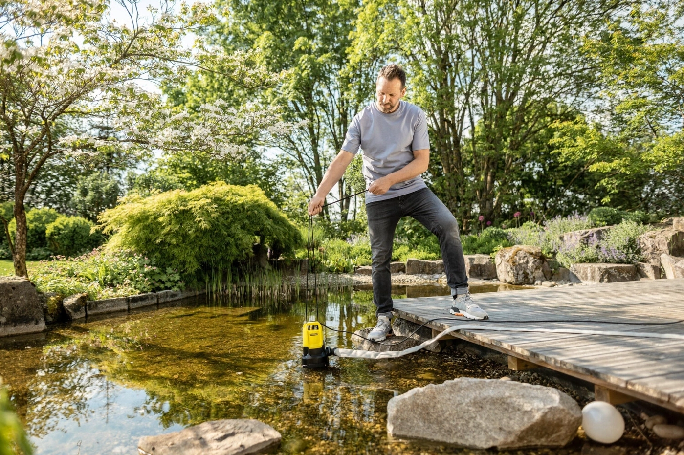 Mann benutzt Wasserpumpe in einem Teich mit Holzsteg