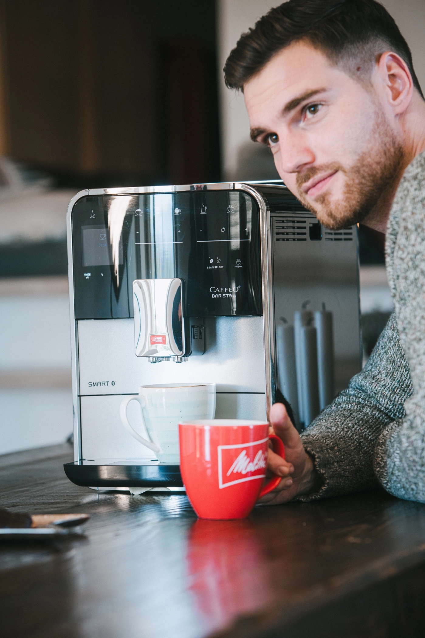 Mann mit Kaffeemaschine und Tasse, die er in der Hand hält, lächelt.