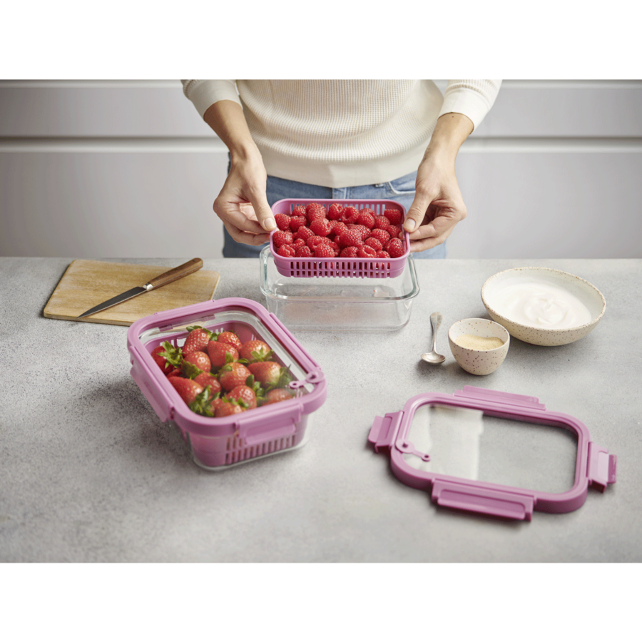Person hält Behälter mit Himbeeren, daneben Erdbeeren und Joghurt