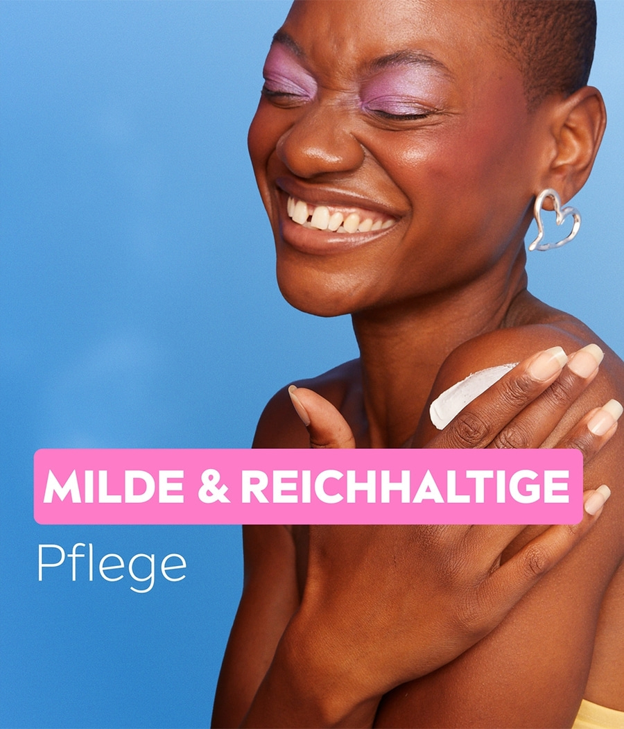 Eine Frau mit lila Lidschatten und Herz-Ohrring lächelt, mit der Aufschrift "Milde & Reichhaltige Pflege".