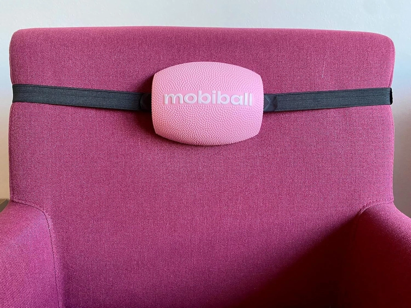 Ein pinkfarbener Stuhl mit einem mobiball-Rückenkissen und einem schwarzen Gurt.