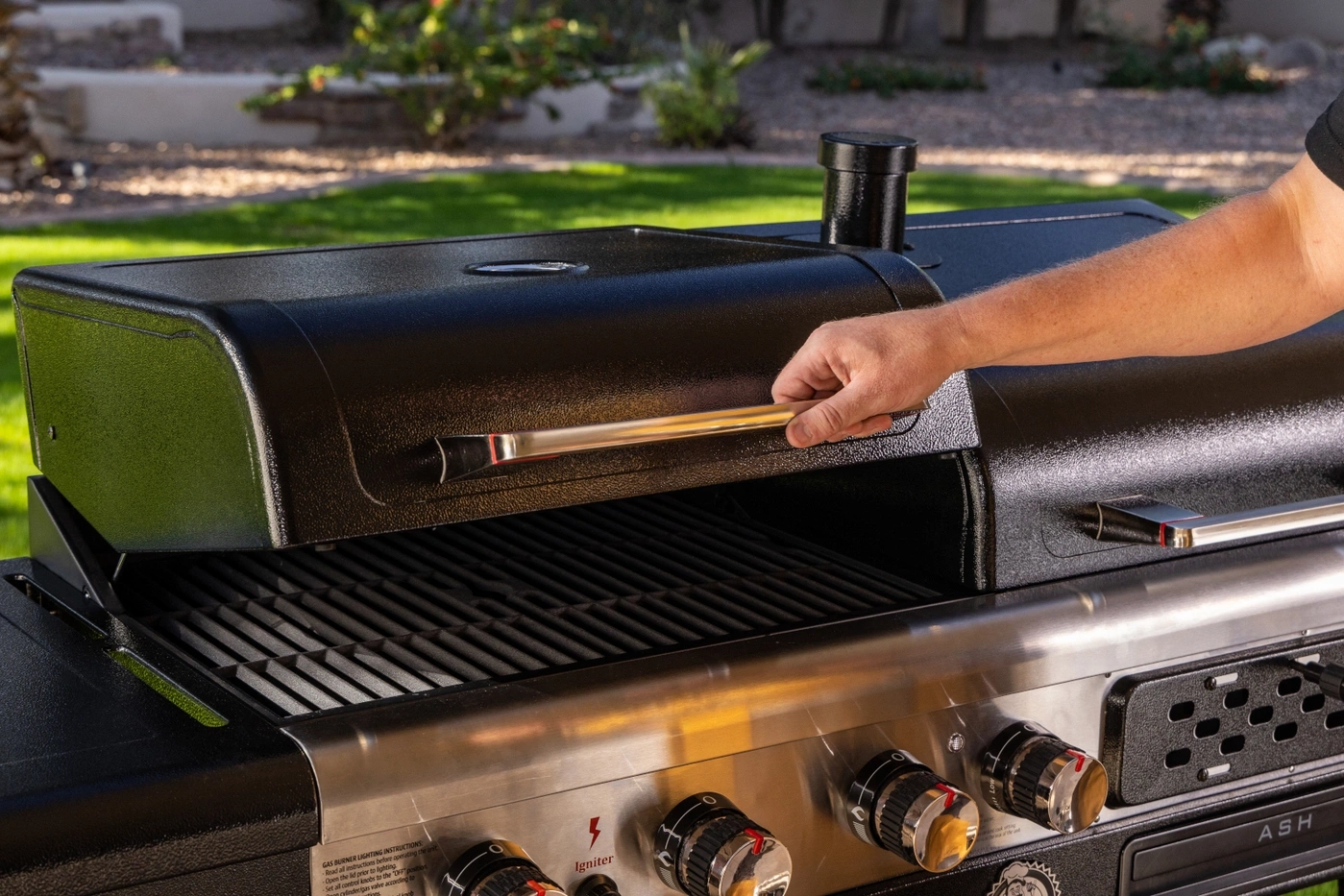 Mann öffnet den Grilldeckel, um die Grillroste zu sehen.