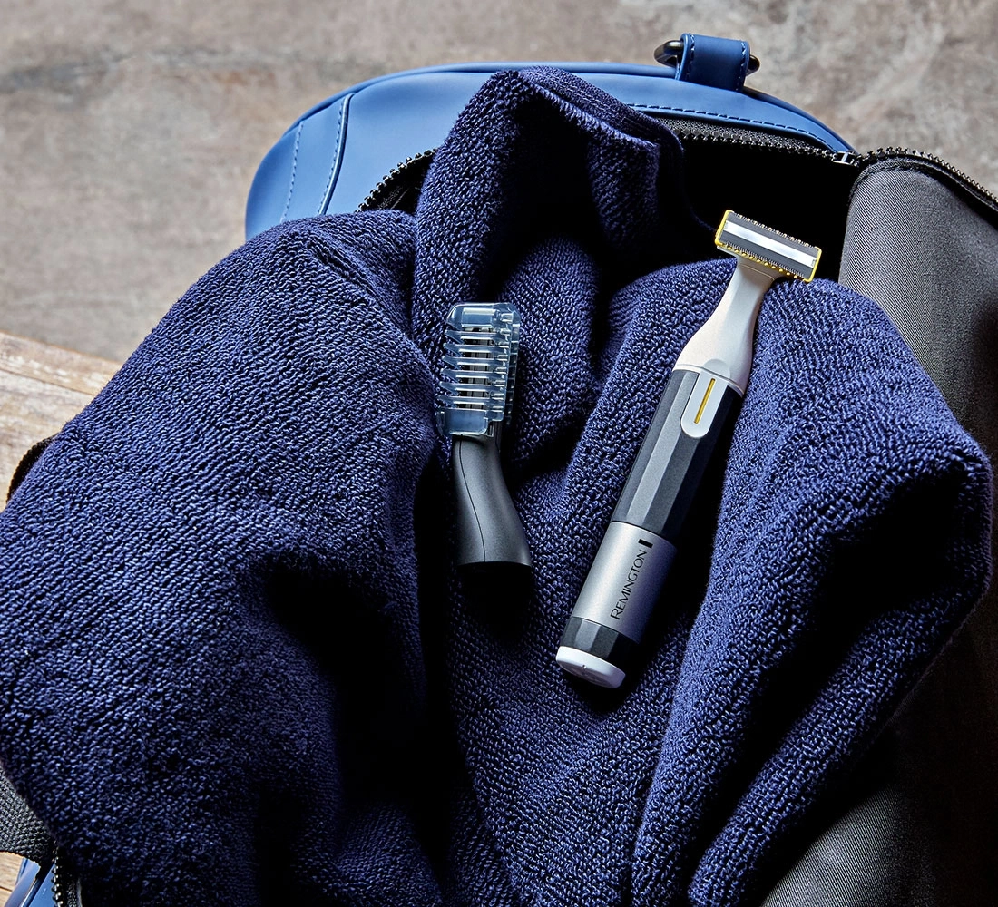 Ein Rasierer und ein Trimmer liegen auf einem blauen Handtuch in einer Tasche.