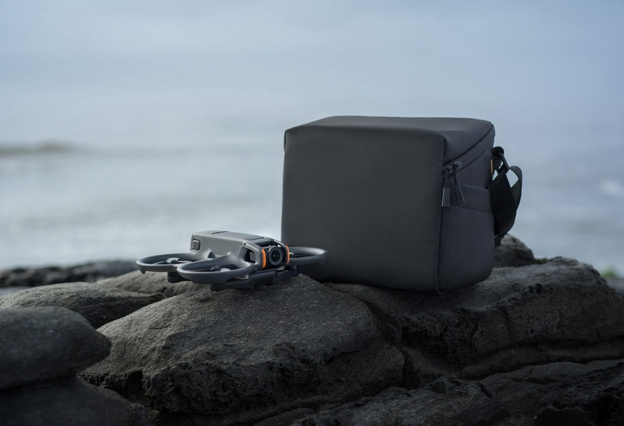 Drohne und Tasche auf einem Felsen am Meer, graue Farben, ruhige Szene.