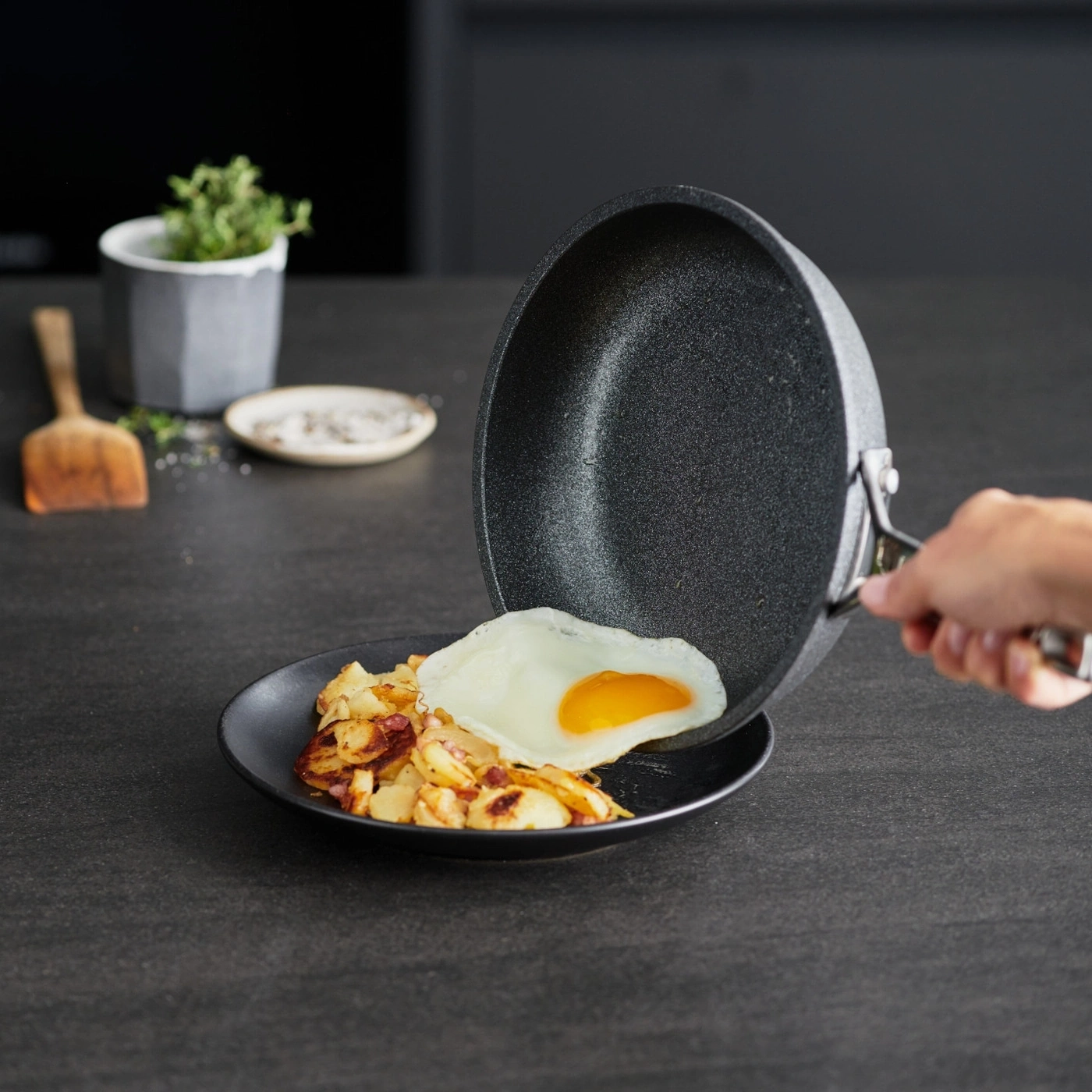 Ein Spiegelei wird aus einer Pfanne auf einen Teller mit Bratkartoffeln gelegt.