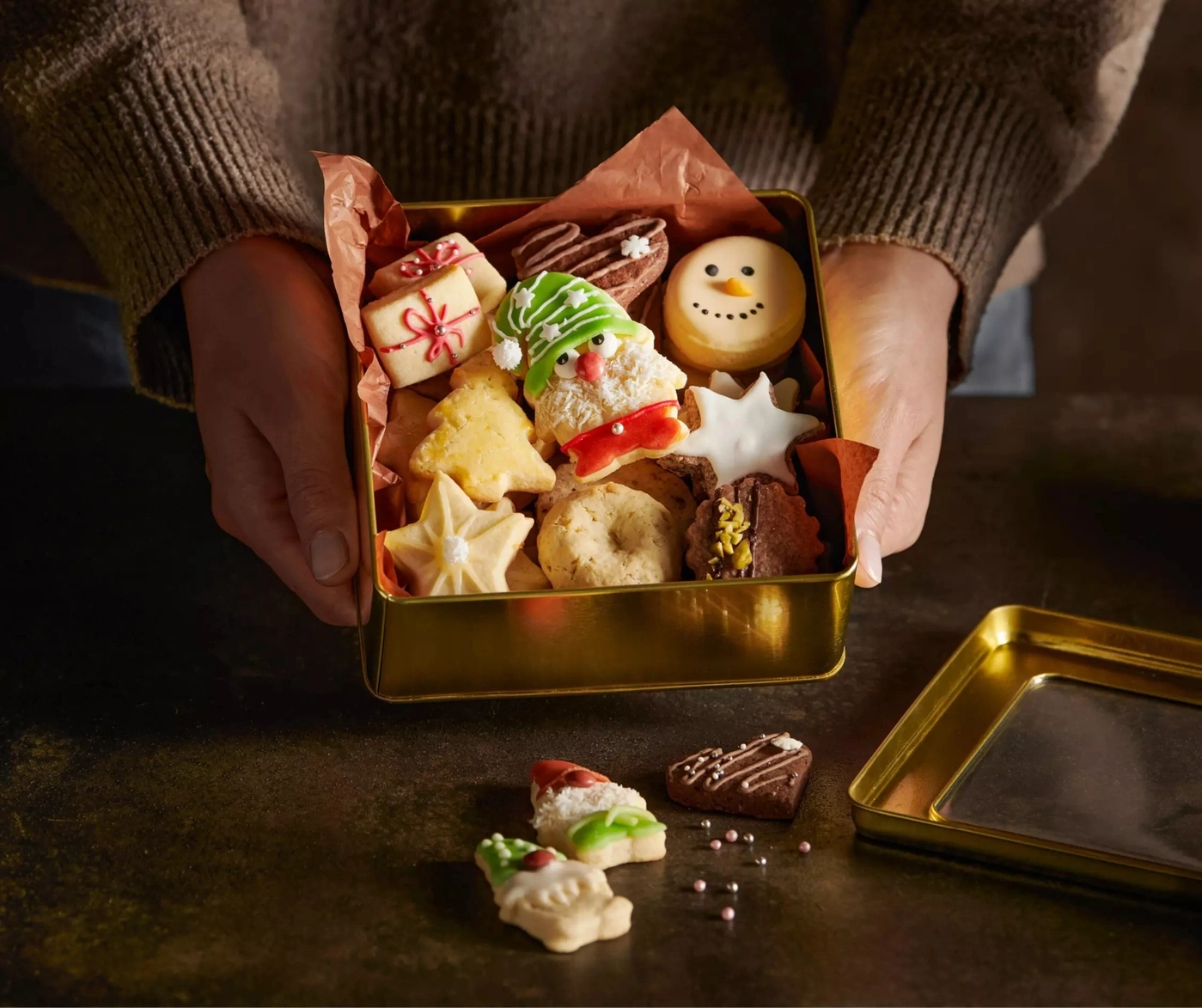 Eine Person hält eine goldene Dose mit Weihnachtsplätzchen.