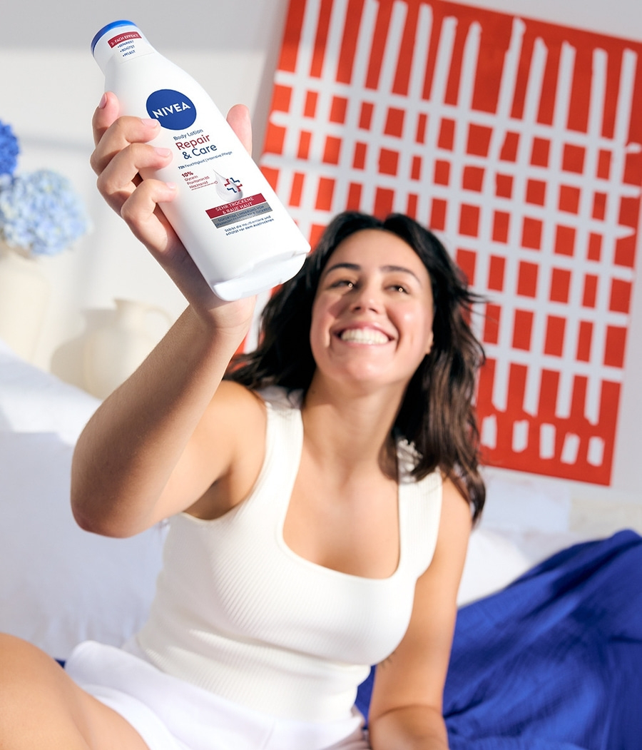 Frau hält Nivea-Körperlotion in die Kamera, lächelt, weißes Top, roter Hintergrund