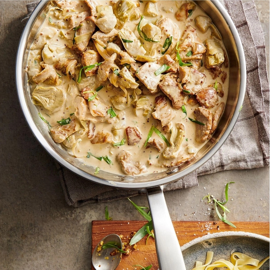 Gericht mit Fleisch, Artischocken und Sauce in einer Pfanne, serviert mit Nudeln.