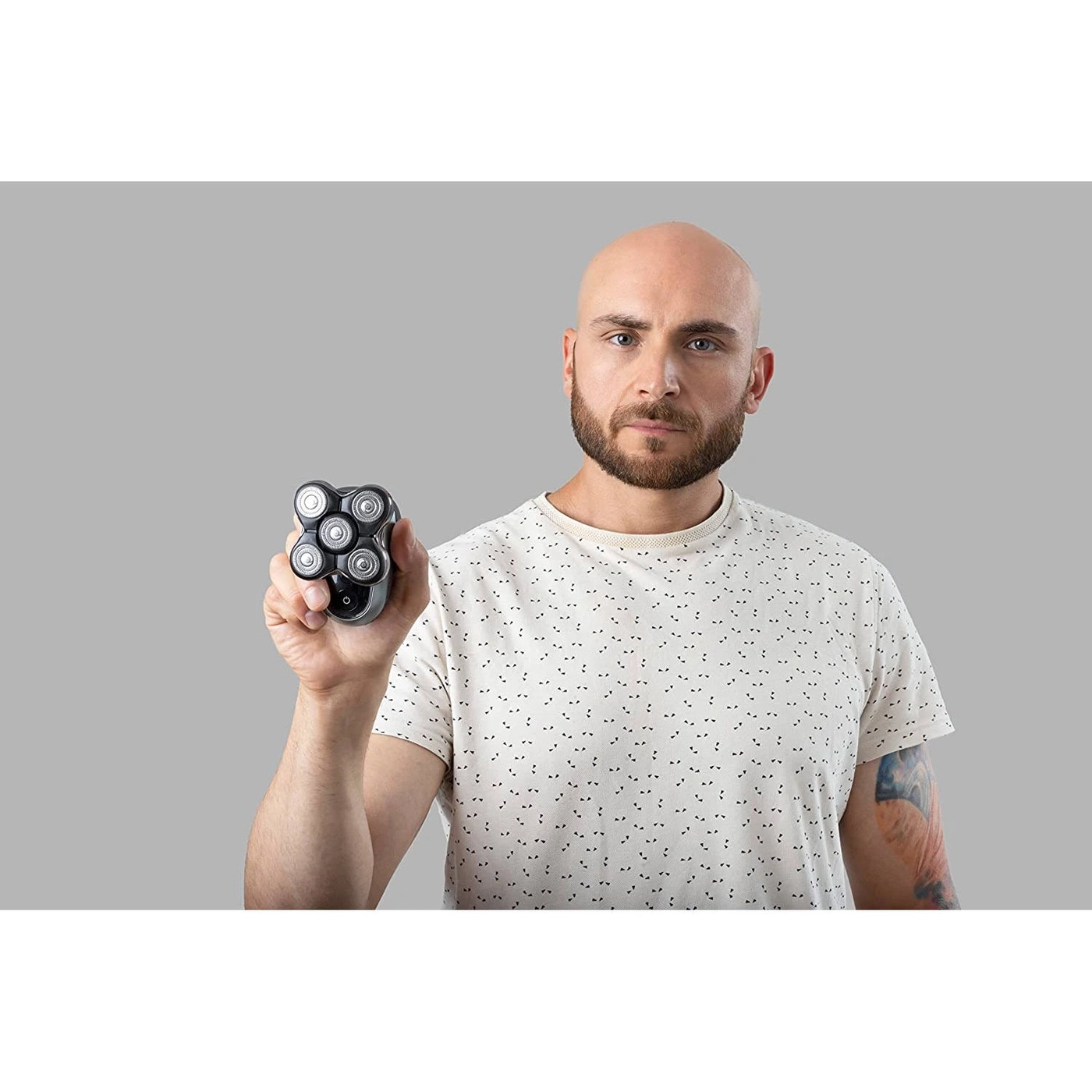 Mann mit Glatze und Bart hält Rasierer in der Hand, grauer Hintergrund