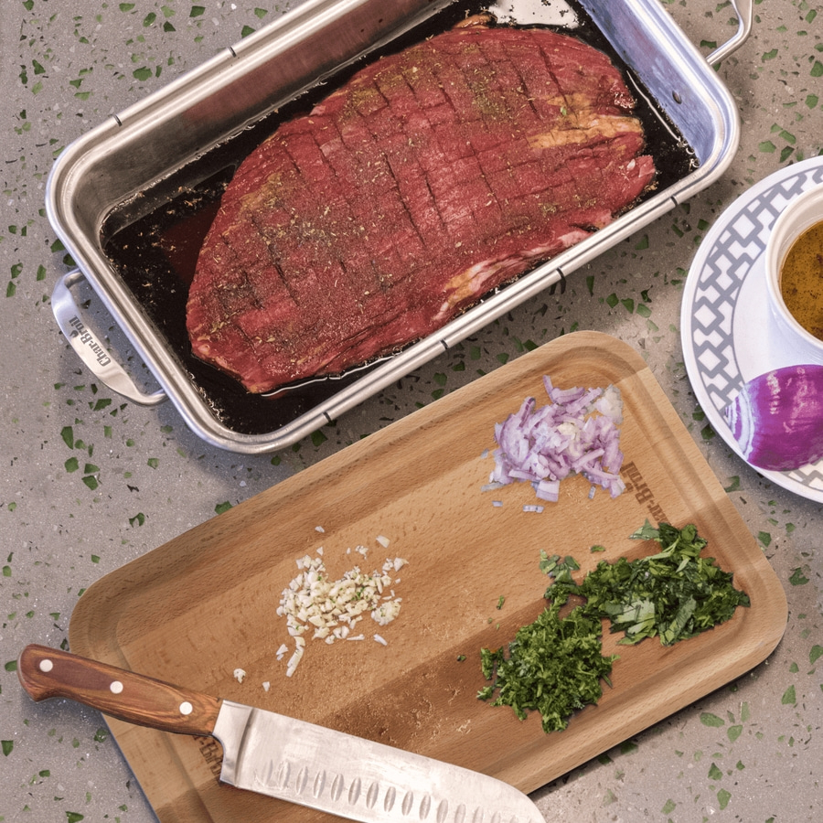 Rohes Fleisch in einer Auflaufform mit Zutaten auf einem Schneidebrett.