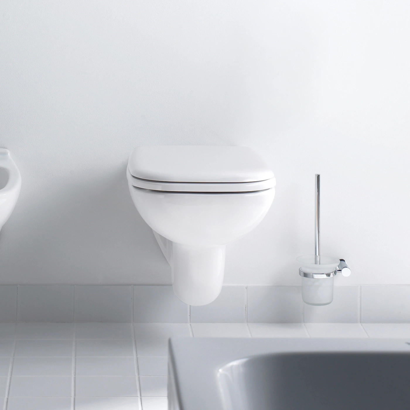 Ein weißes Wand-WC und ein Bidet neben einem schmutzigen Badezimmer.