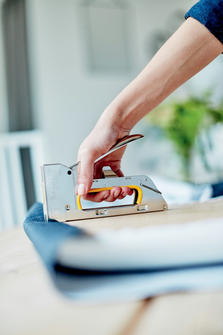 Eine Hand benutzt einen Tacker, um Stoff an Holz zu befestigen.