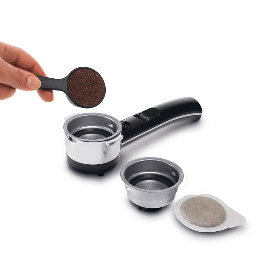 Eine Hand hält einen Löffel mit Kaffeepulver über einen Siebträger, daneben liegen ein weiteres Sieb und ein Kaffeepuck.