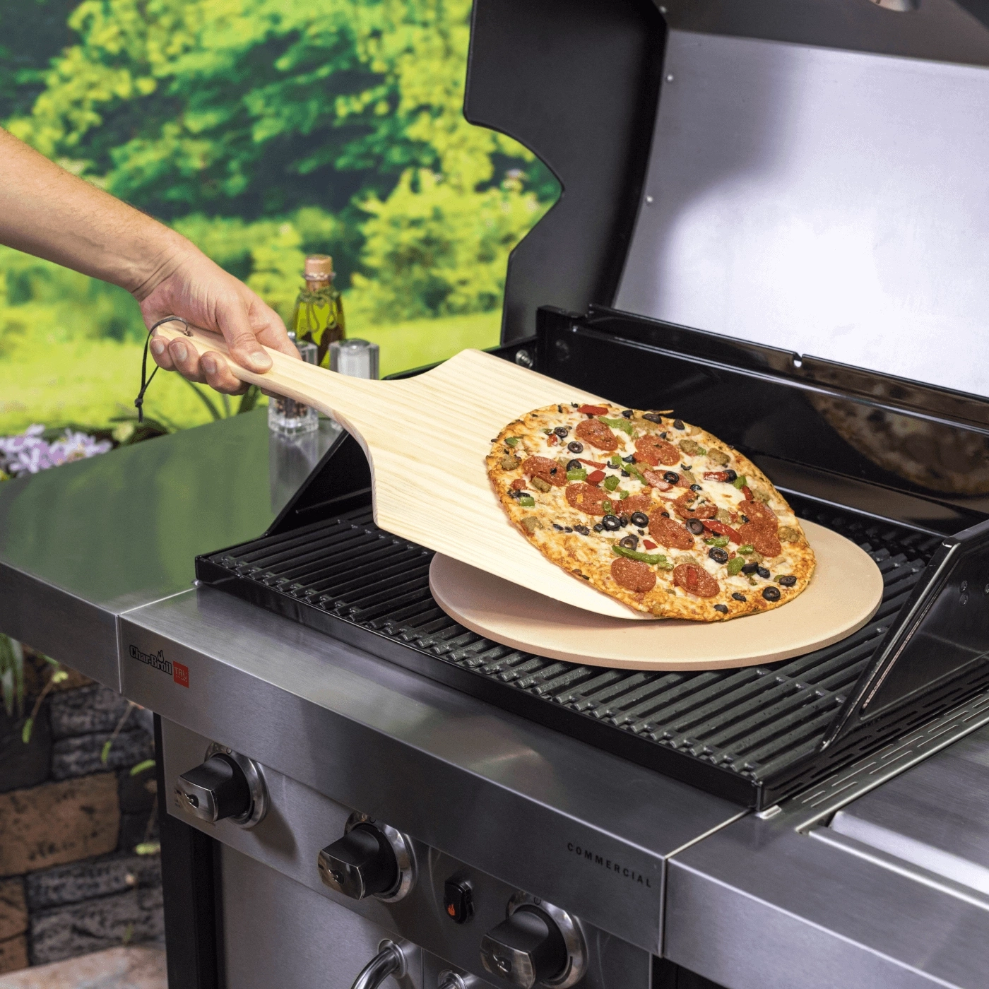 Pizza wird auf einem Grill mit Pizzastein und Schaufel zubereitet.