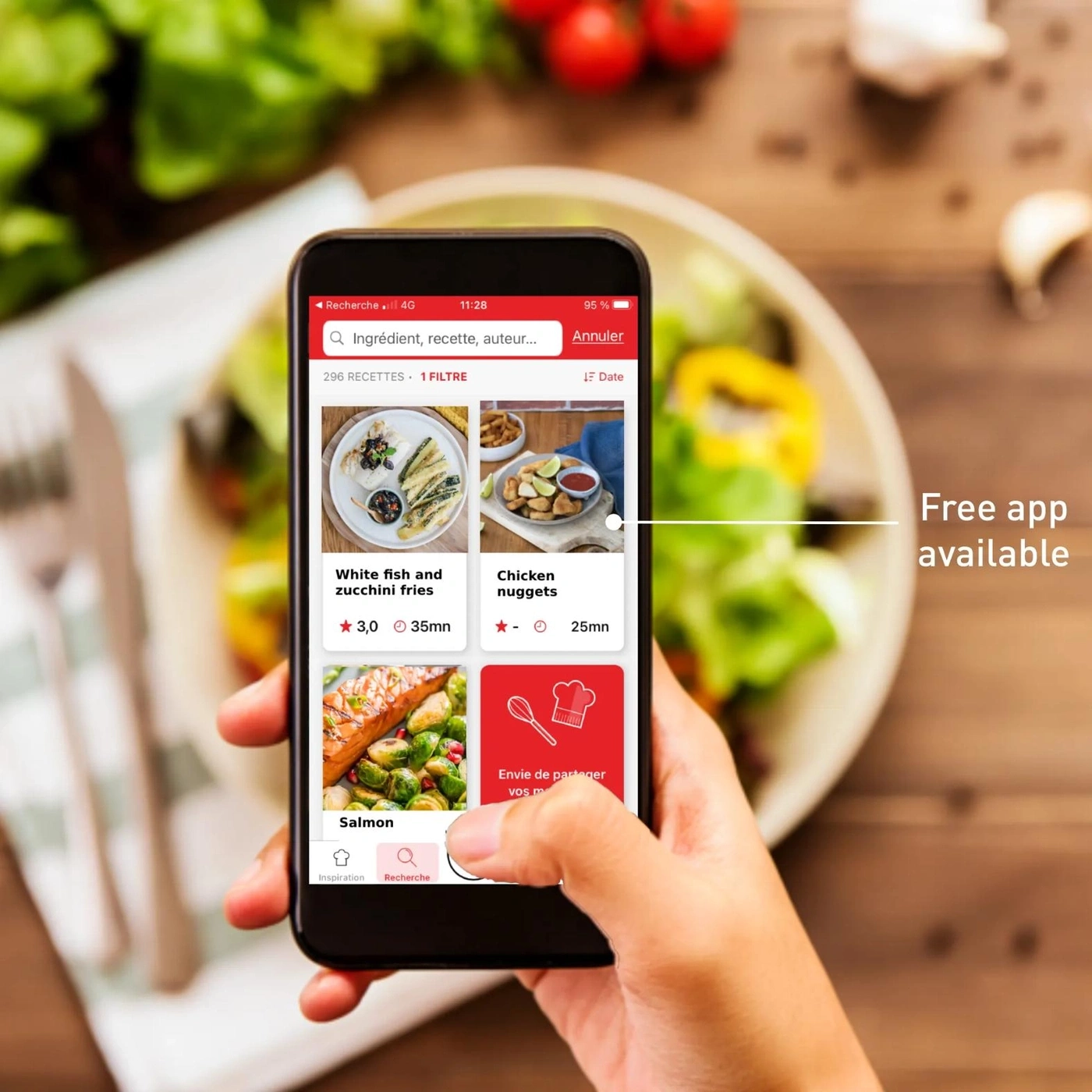 Eine Hand hält ein Smartphone mit einer Kochrezept-App, auf der ein Lachsgericht und ein Salat zu sehen sind.