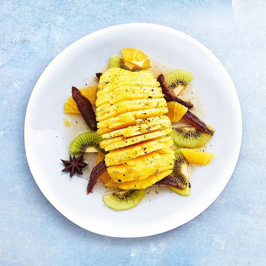 Teller mit Ananas, Kiwi, Orange und Gewürzen, auf blauem Hintergrund