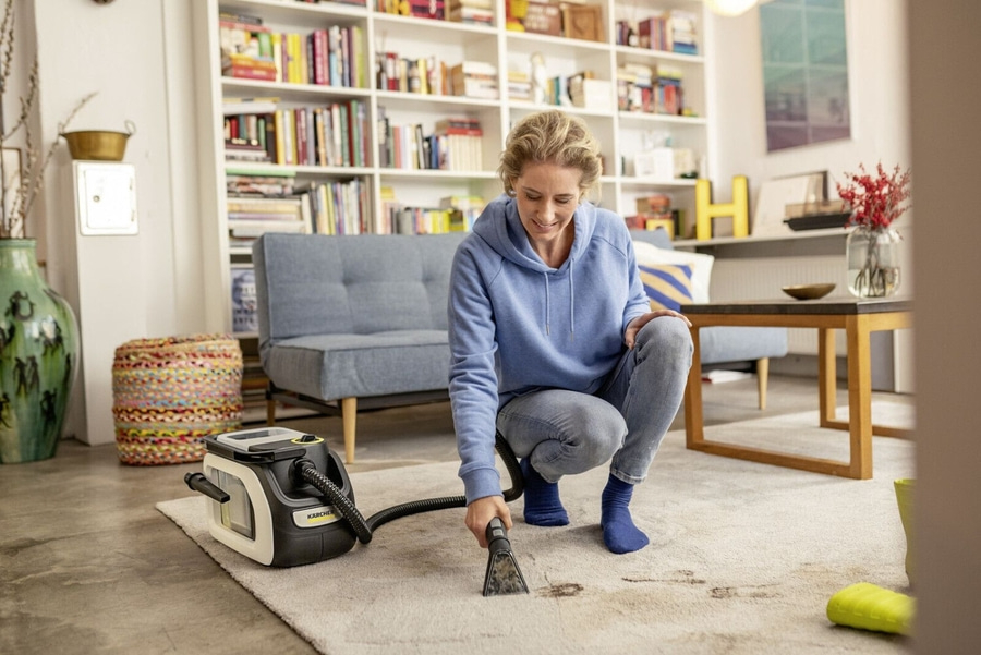 Frau reinigt Teppich mit Staubsauger im Wohnzimmer, lächelt.