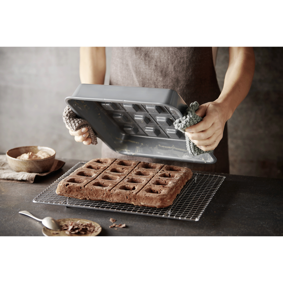 Person hält Backform über Kuchen, der auf einem Rost liegt, mit Zutaten.