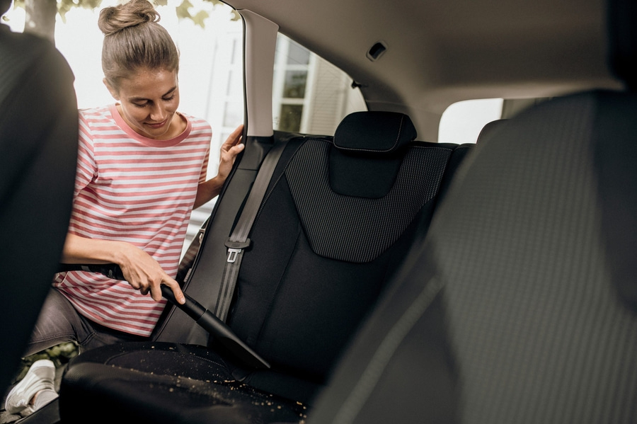 Frau saugt Auto aus, um es zu reinigen, mit Staubsauger und Sitz