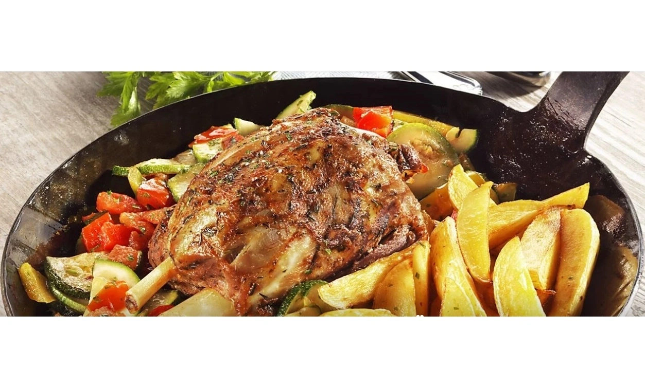 Gebratenes Fleisch mit Kartoffelspalten und Gemüse in einer Pfanne.
