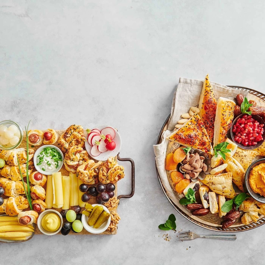 Zwei Platten mit verschiedenen Snacks, Käse, Obst und Gemüse.