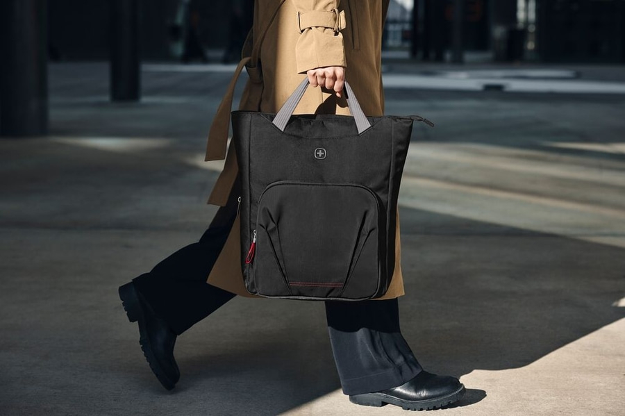 Person trägt schwarze Tasche mit grauem Griff, geht auf dem Bürgersteig.