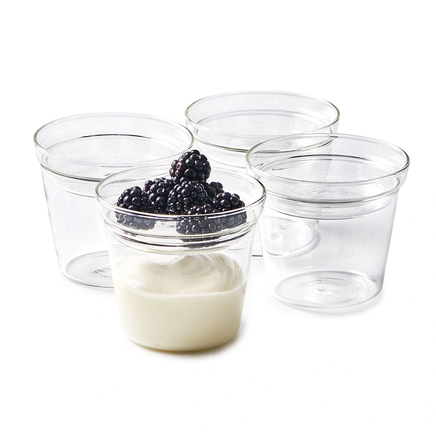Vier leere Gläser und ein Glas mit Joghurt und Brombeeren