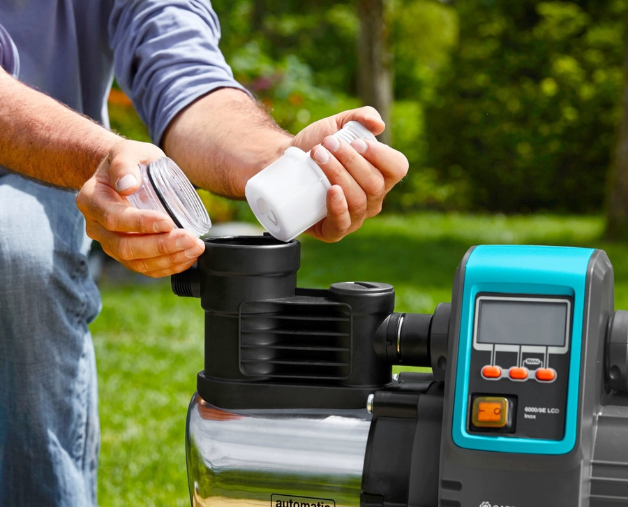 Mann montiert Wasserpumpe im Garten, mit Filter und Display.