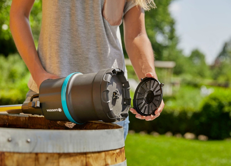 Person hält ein schwarzes Gerät mit blauem Ring und einem Filter in der Hand, im Garten.