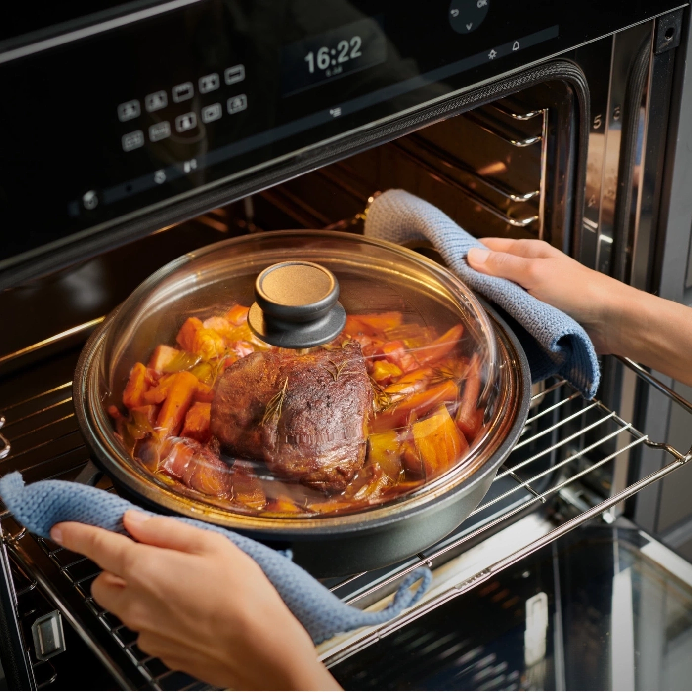 Ein Braten im Ofen mit Gemüse, wird mit Handschuhen herausgenommen.