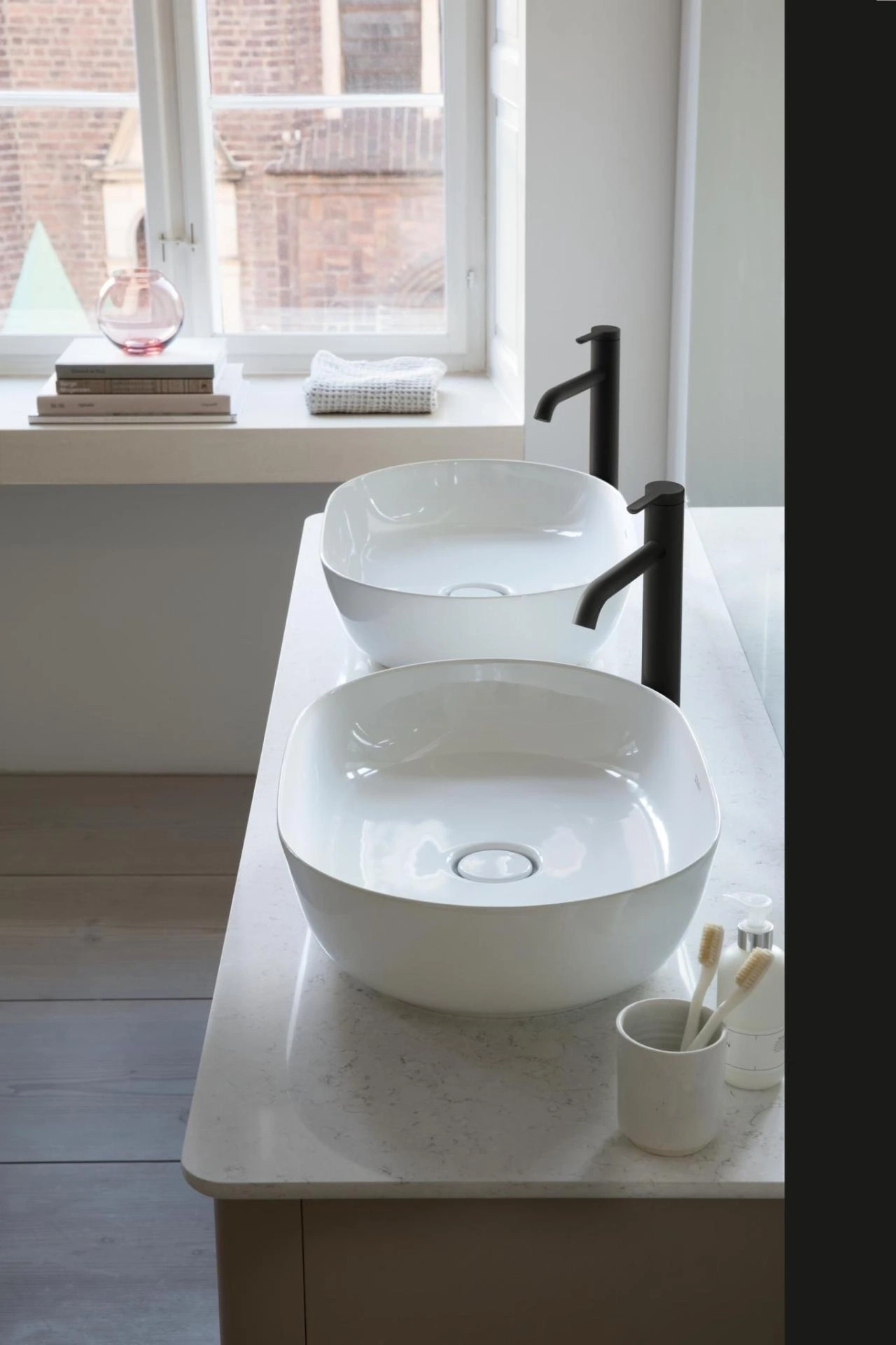 Zwei weiße Waschbecken mit schwarzen Wasserhähnen in einem Badezimmer mit Fenster.