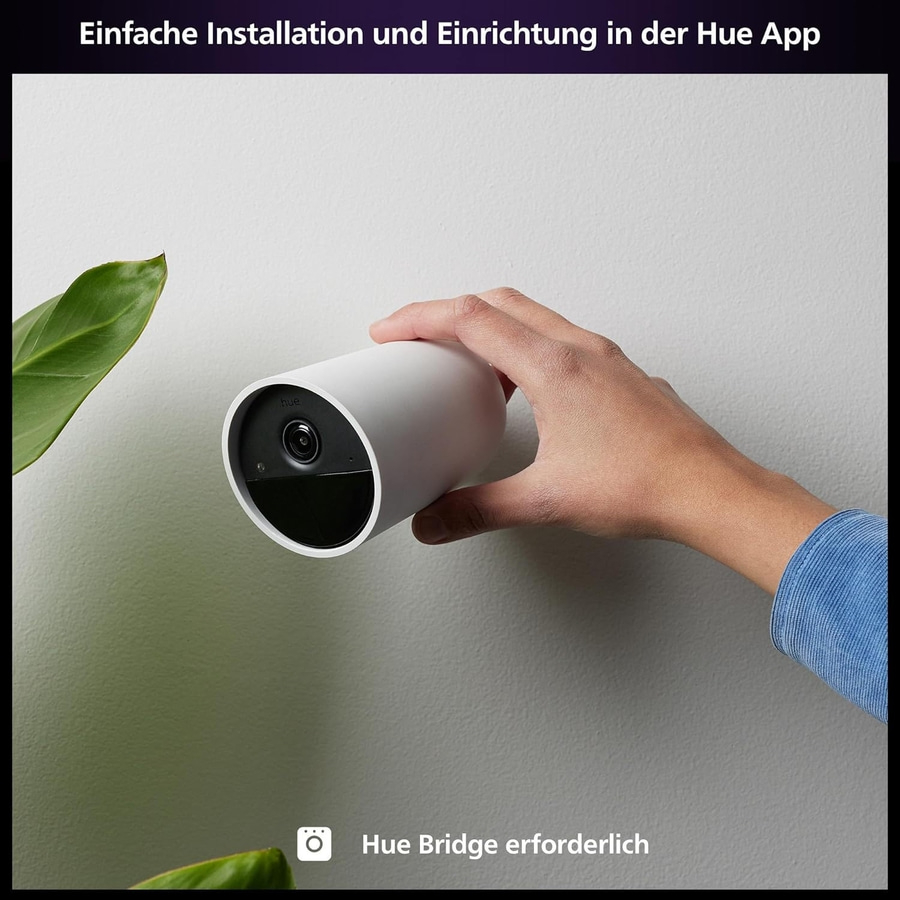 Person hält eine weiße Kamera. Einfache Installation in der Hue App. Hue Bridge erforderlich.