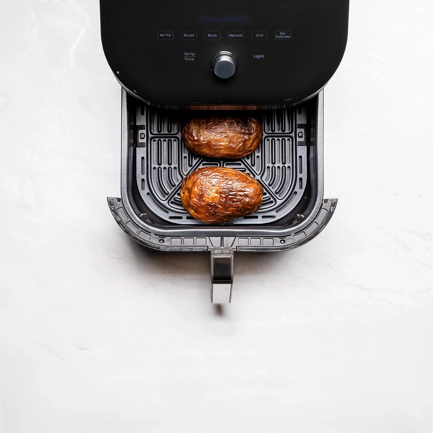 Zwei gebackene Kartoffeln in einem schwarzen Airfryer auf Marmoruntergrund