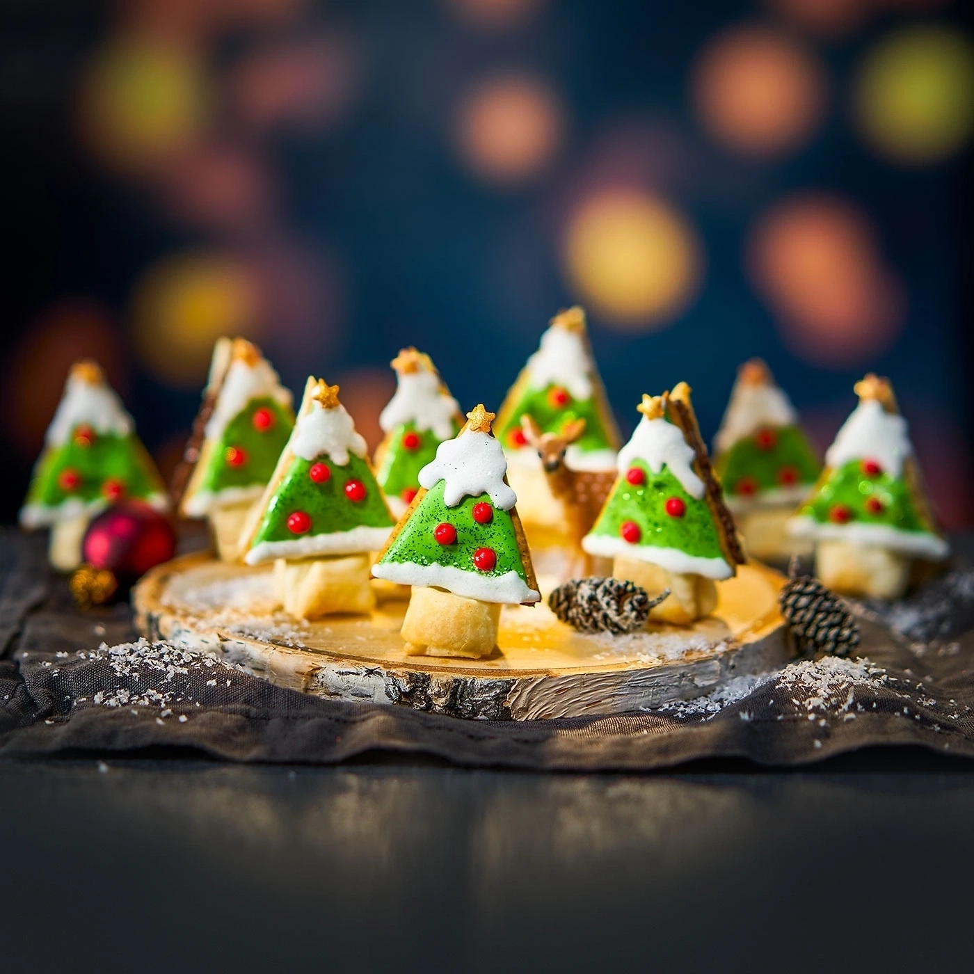 Weihnachtsbäume aus Keksen auf einem Holzbrett mit Dekoration und Bokeh-Effekt.