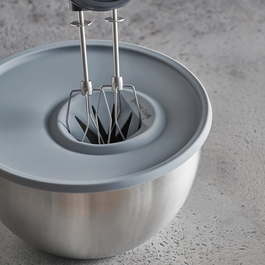 Edelstahlschüssel mit Handrührgerät, grauem Deckel und Betonhintergrund