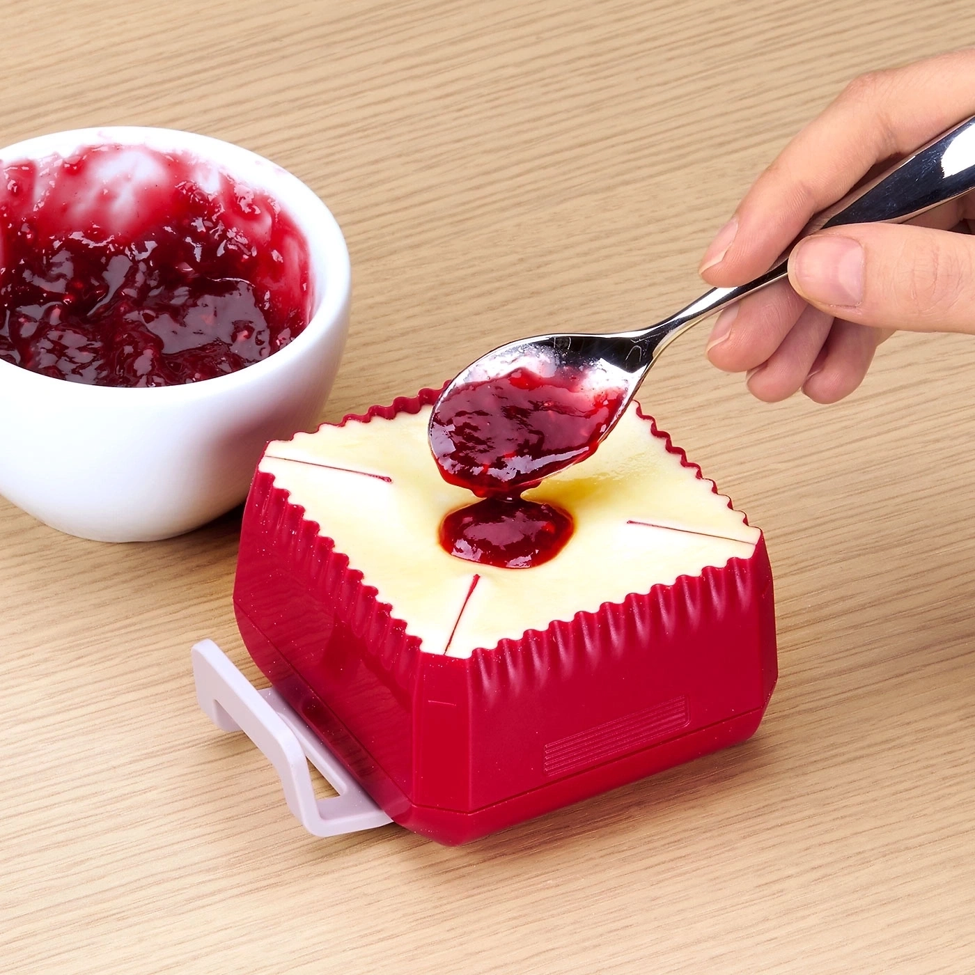 Jemand gibt Marmelade auf ein Stück Käse mit einem Löffel.