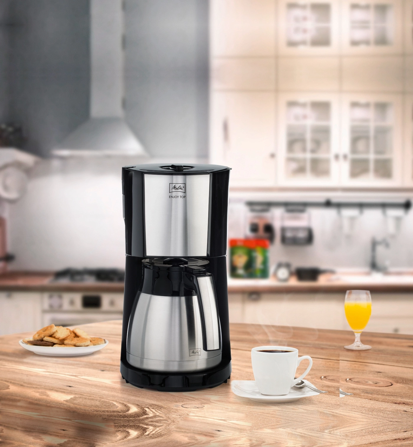 Kaffeemaschine mit Tasse Kaffee, Saft und Keksen auf einem Holztisch in der Küche