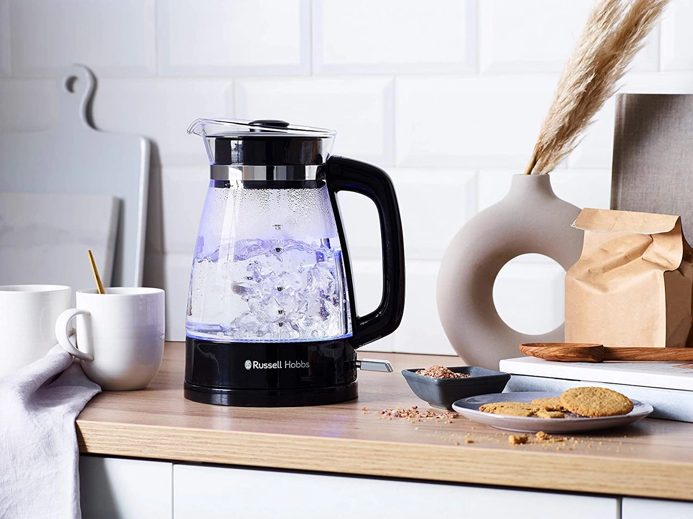 Wasserkocher mit Wasser, Tassen, Keksen und Dekoration auf einem Tisch