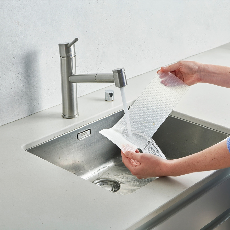 Person wäscht ein weißes, strukturiertes Pad unter fließendem Wasser in der Spüle.