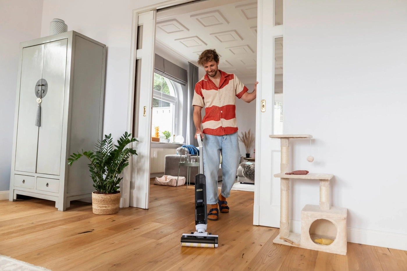 Ein Mann saugt den Holzboden mit einem kabellosen Staubsauger