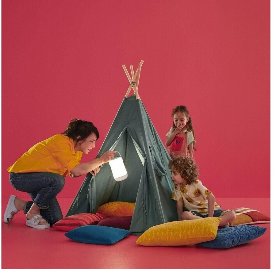 Frau und Kinder spielen in einem Zelt mit einer Lampe auf rotem Hintergrund