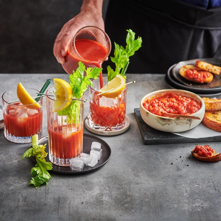 Bloody Marys mit Tomaten-Toasts, Zitrone und Sellerie auf grauem Tisch