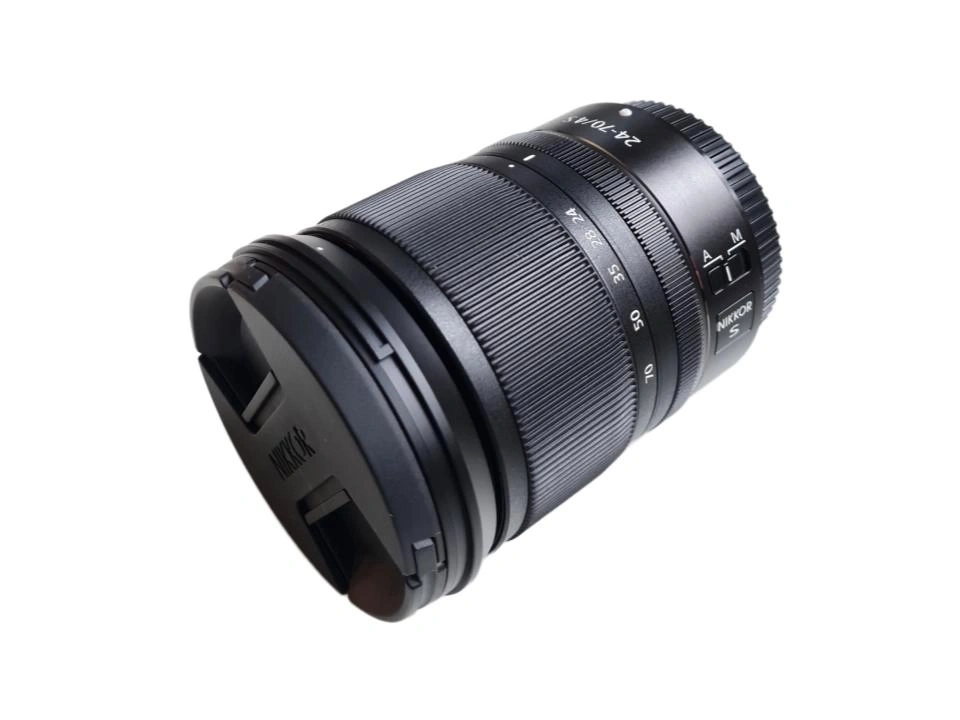 Eine schwarze Nikon NIKKOR Z 24-70mm f/4 S Kameraobjektivlinse, mit Frontdeckel, auf weißem Hintergrund.