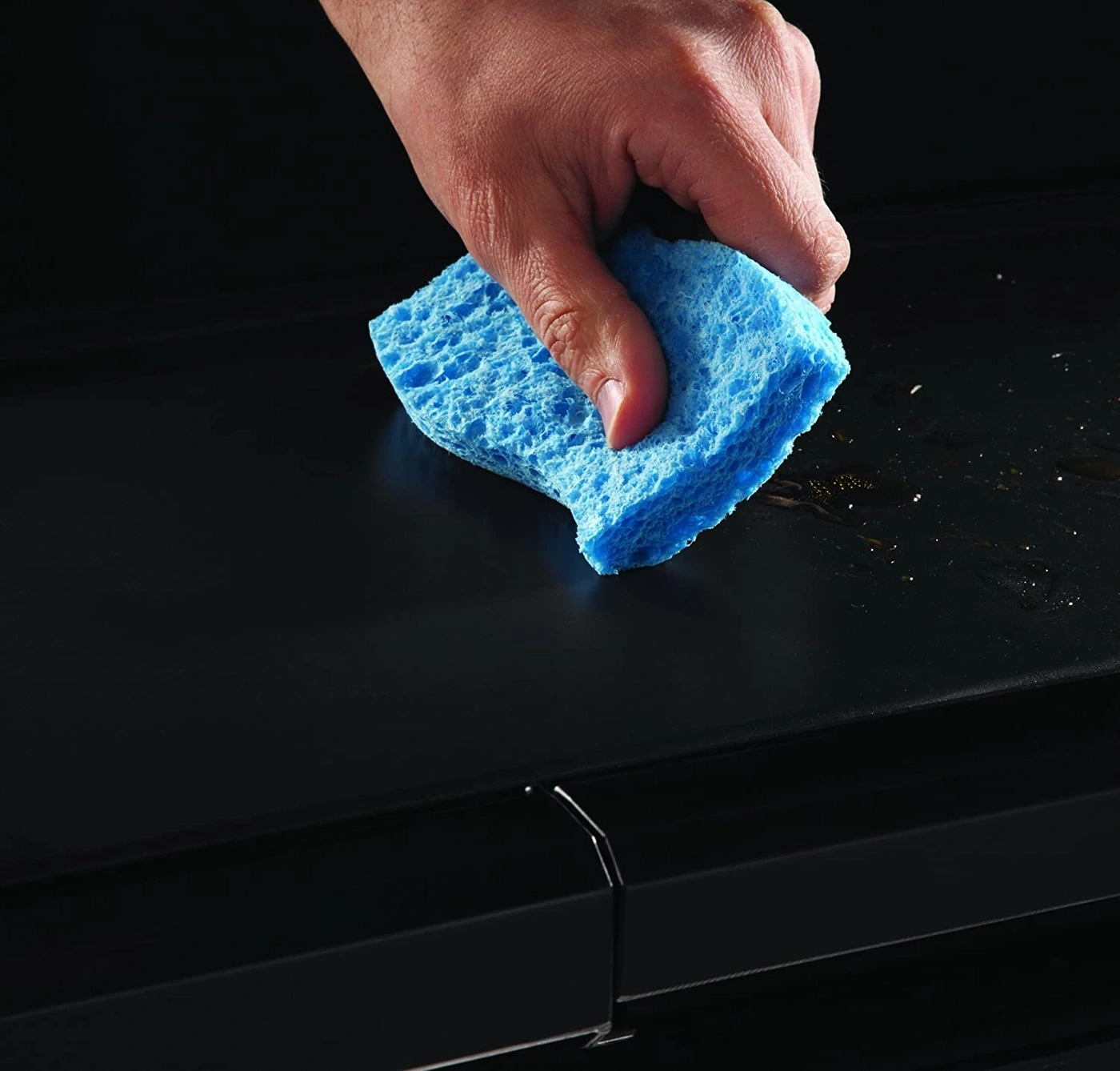 Hand reinigt schwarze Oberfläche mit blauem Schwamm, Nahaufnahme