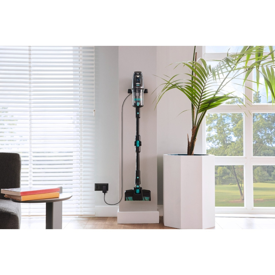 Ein moderner Staubsauger lädt an einer Wandhalterung neben einem Fenster und einer Pflanze.
