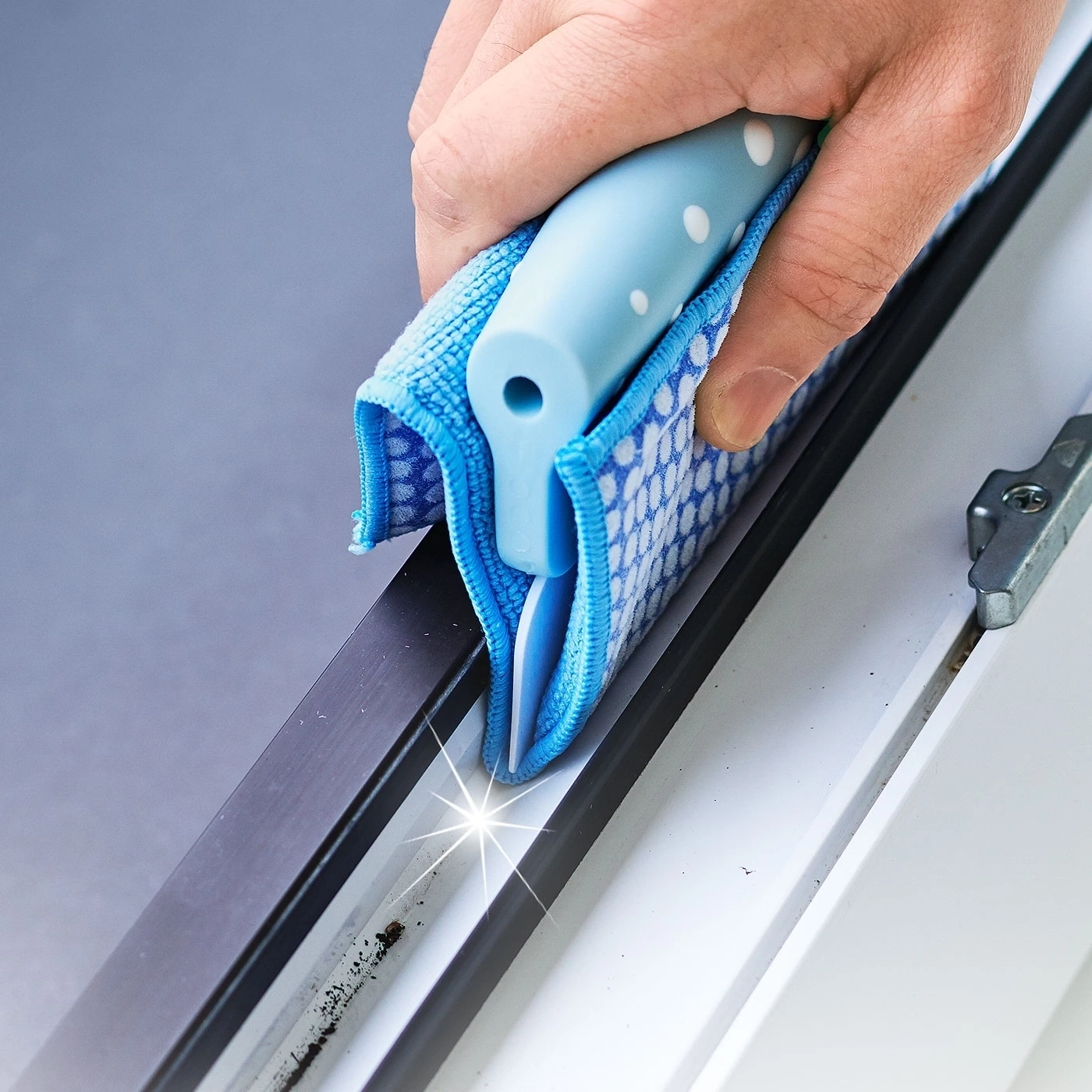 Hand reinigt Fensterrahmen mit blauem Reinigungswerkzeug und Tuch