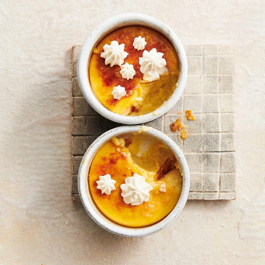 Zwei Crème brûlée in Schalen mit Sahne dekoriert, auf einem quadratischen Untersetzer