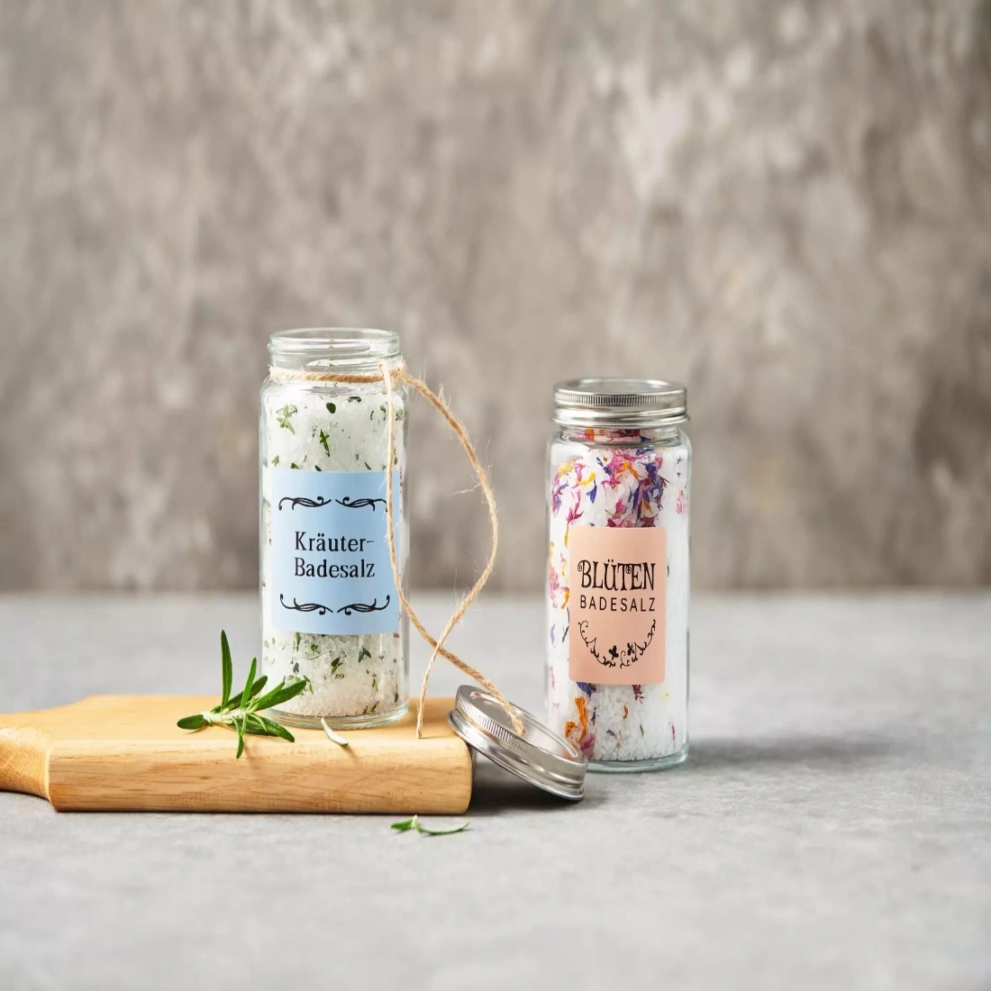 Zwei Gläser mit Badesalz, eines mit Kräutern, eines mit Blüten.
