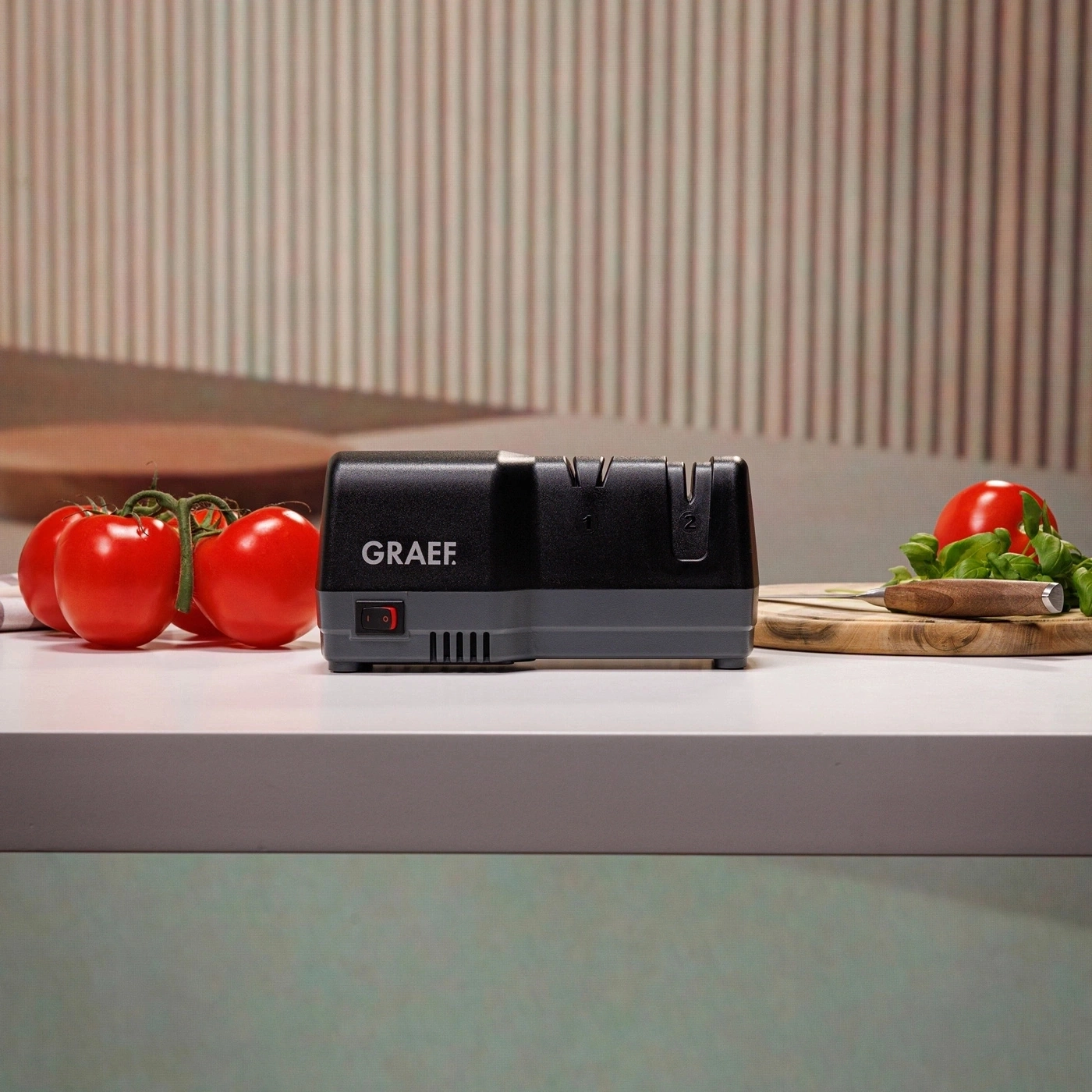 Ein elektrischer Messerschärfer von Graef mit Tomaten und Kräutern auf einem Tisch